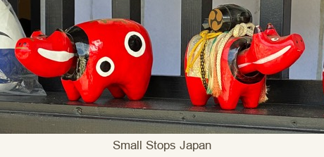 Two red akabeko with separate heads sitting within dark openings at the front of their bodies.