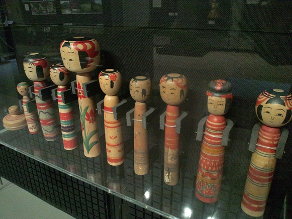 A museum display of Tsuchiyu-type wooden dolls with different faces, concentric crown rings and painted cylindrical bodies.
