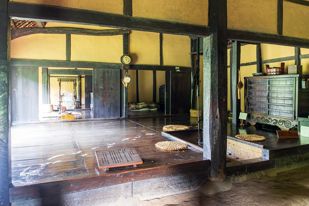A raised wooden floor, dark timber posts and round woven seats inside the Former Narawa Family House.