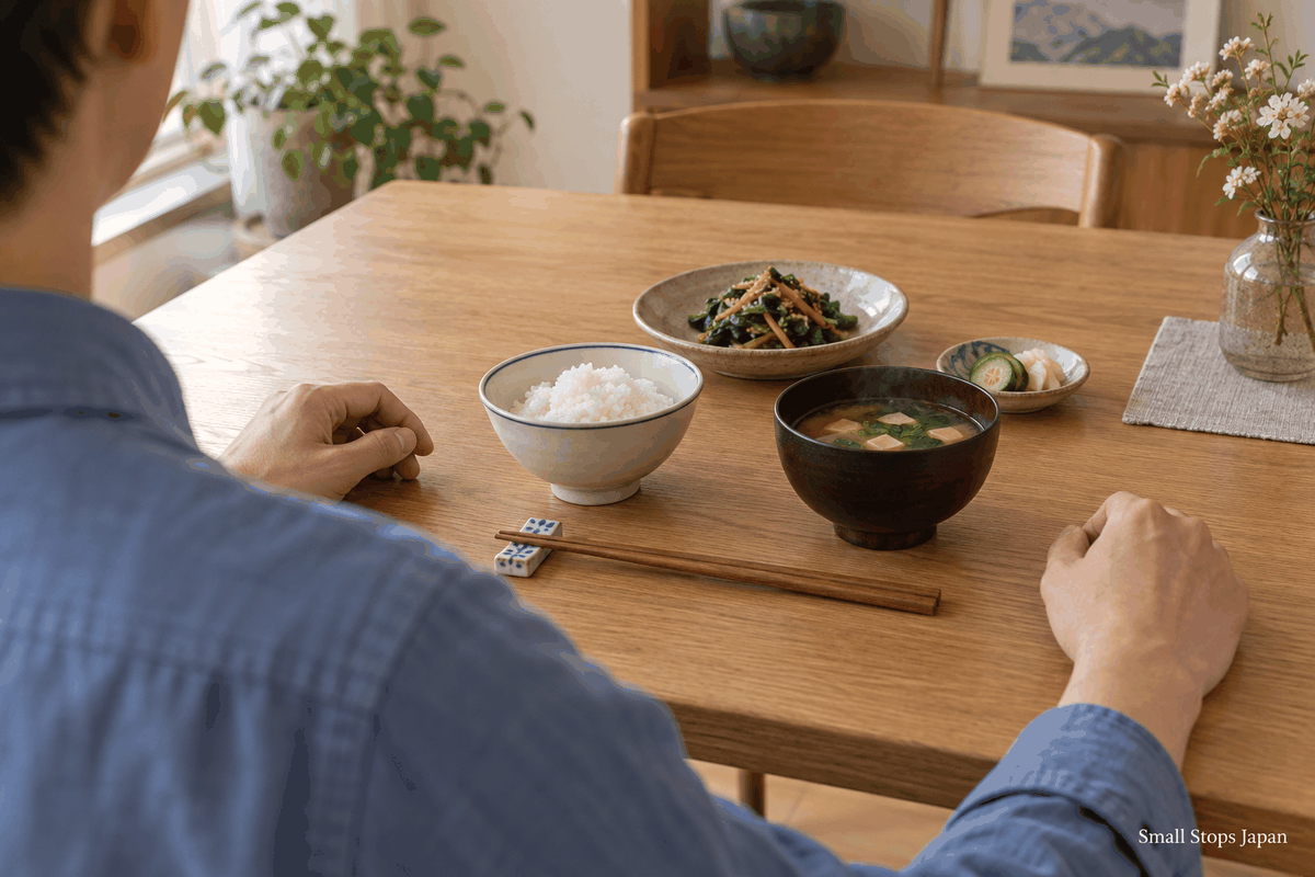 An illustrated meal with the rice bowl back on the table, soup beside it, and chopsticks laid on a rest.