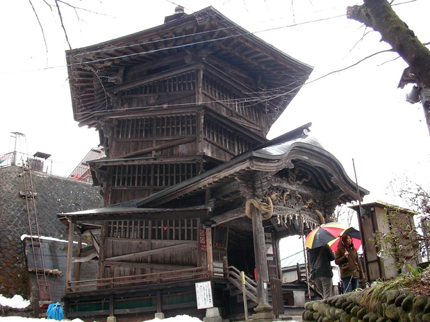The multi-level wooden Sazaedo hall and its projecting entrance roof, with visitors near the doorway.