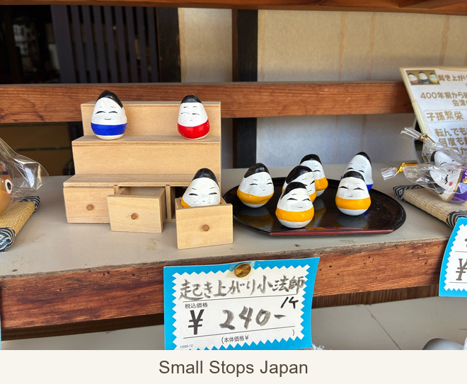 Rounded red, blue and yellow okiagari koboshi displayed on wooden steps and a tray.