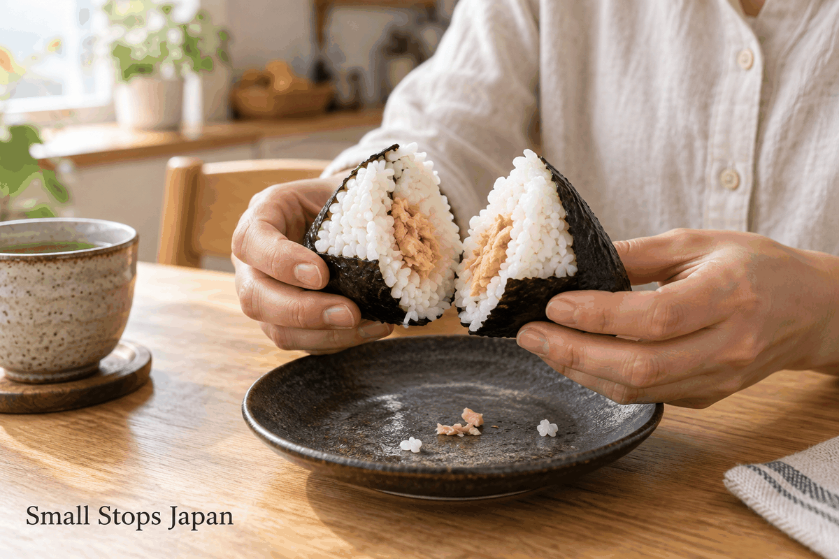 Hands hold two halves of a rice ball, showing cooked rice around a salmon filling.