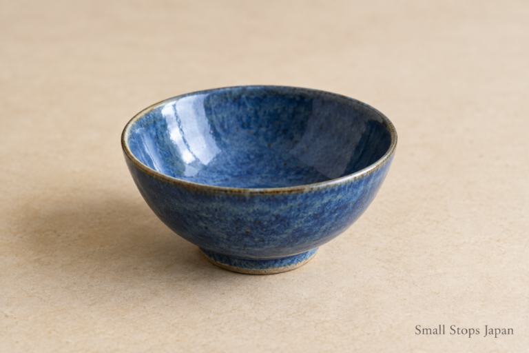 An empty blue ceramic bowl with its rim, curved interior and small foot visible.