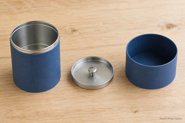 An open blue tea canister with a separate shallow silver inner lid and a deeper blue outer lid.