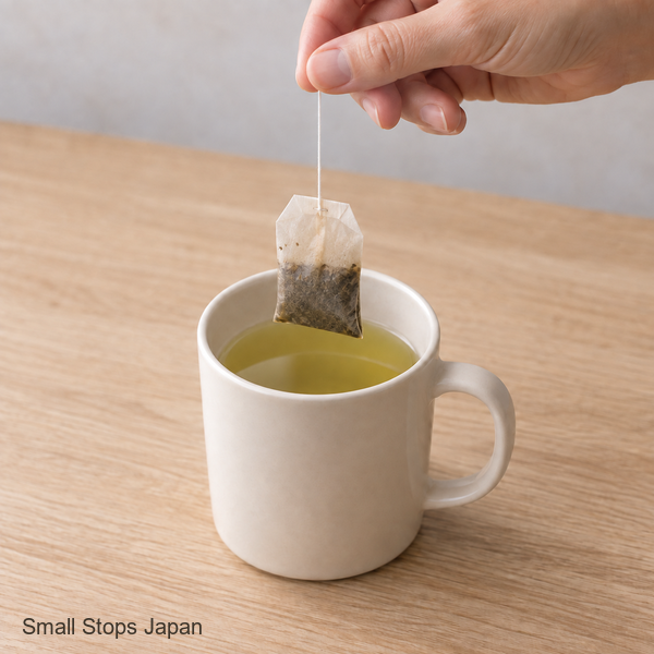A hand lifts a tea bag by its string from a mug of tea.