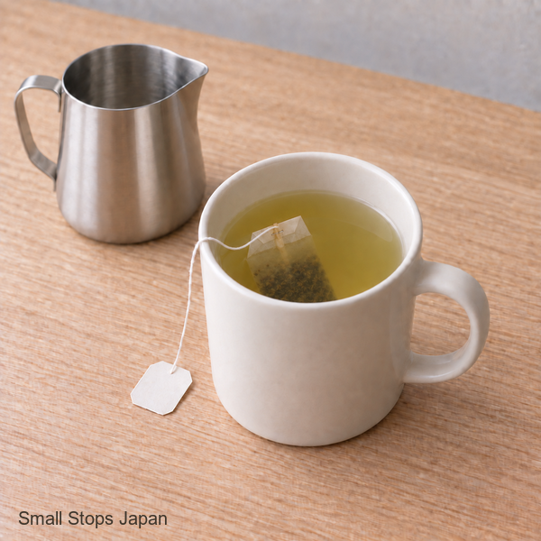 Illustration of a tea bag in an ivory mug of tea, with its string draped over the rim and a steel jug resting nearby.