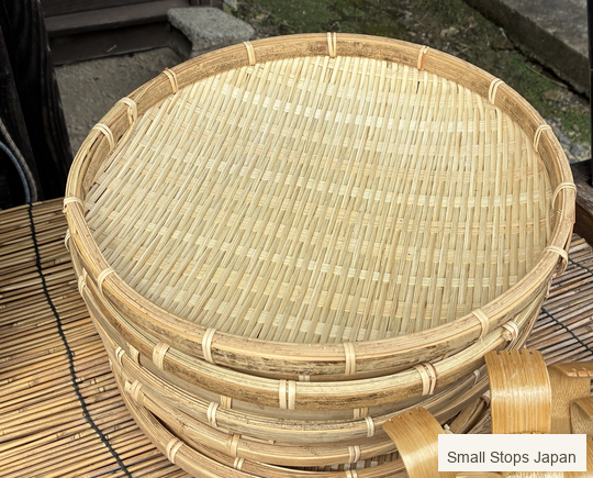 Shallow round woven baskets stacked at an Ouchi-juku shop, showing a broad woven face and bound rim.