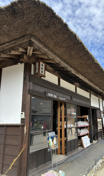 Oblique view along a thatched eave towards a shopfront and its entrance.