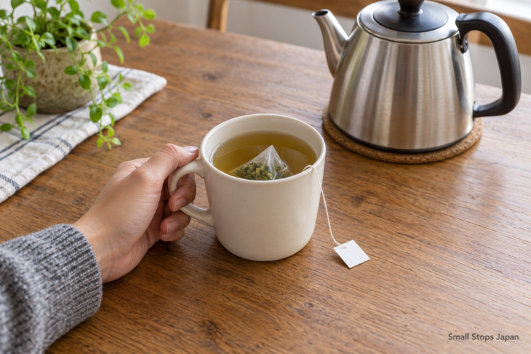 A hand holds a mug with a tea bag and string, with a kettle nearby.