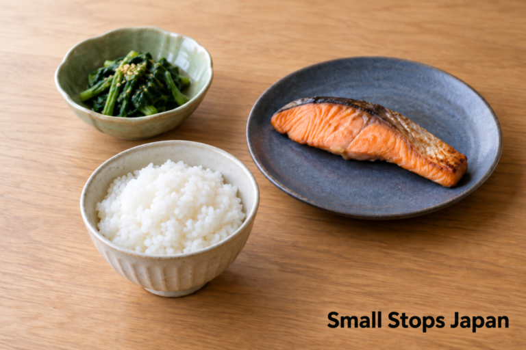 Plain rice in a bowl, grilled fish on a plate and greens in a small bowl, with space between the three vessels.