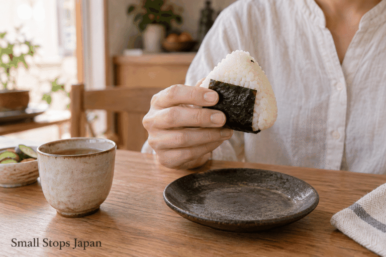 A hand supports an onigiri with nori around the rice, above a plate.