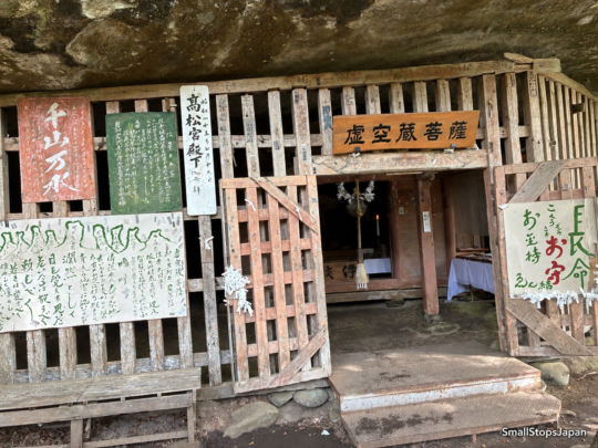 A wooden entrance beneath a rock overhang, with a sign reading Kokuzo Bosatsu above the doorway.