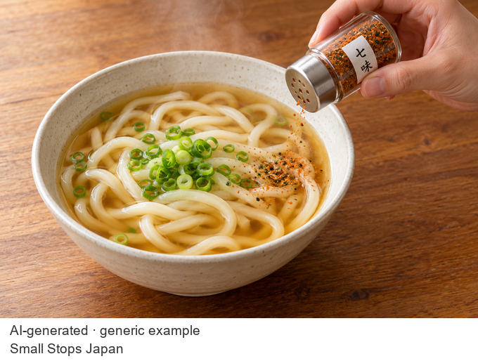 AI-generated hand tilting a shichimi shaker to sprinkle a little seasoning onto one side of an udon bowl.